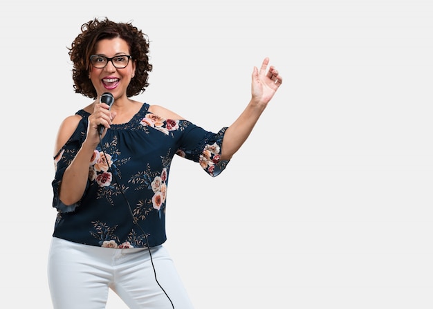 Mujer de mediana edad, feliz y motivada, cantando una canción con un micrófono, presentando un evento o haciendo una fiesta, disfruta el momento.