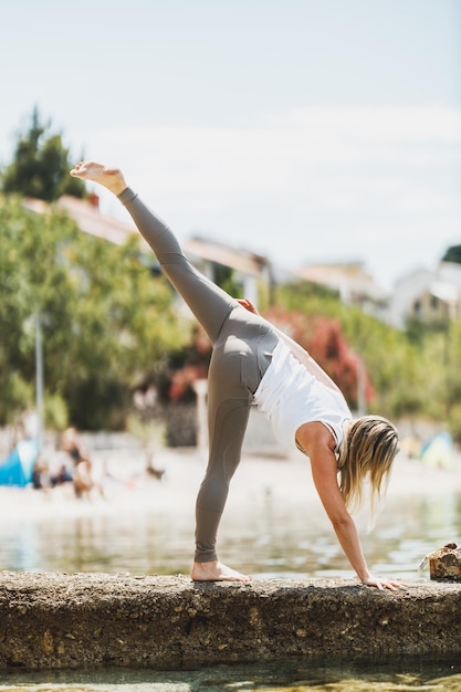 Mujer de mediana edad en forma haciendo ejercicios de yoga durante el entrenamiento cerca de la playa del mar.