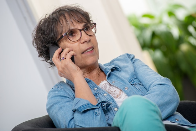 Mujer de mediana edad con gafas feliz hablando con teléfono