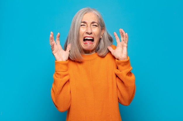 Mujer de mediana edad gritando furiosamente, sintiéndose estresada y molesta con las manos en alto diciendo por qué yo