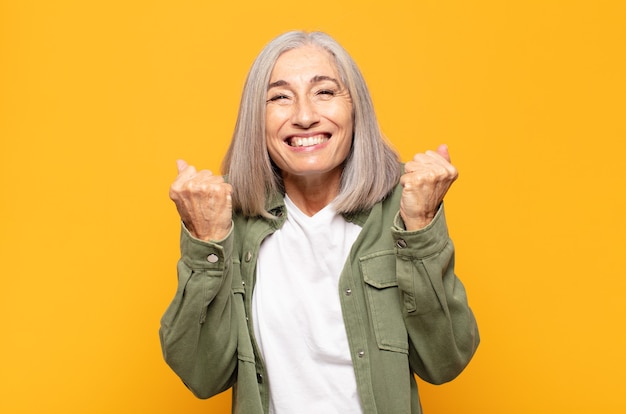 Mujer de mediana edad gritando triunfalmente, riendo y sintiéndose feliz y emocionada mientras celebra el éxito