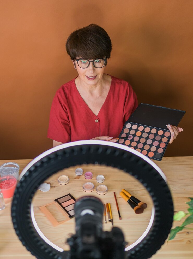 Foto mujer de mediana edad hablando de cosméticos con sombras de ojos de maquillaje y paleta de rubor y pinceles mientras graba su video mujer madura haciendo video para su blog sobre cosméticos