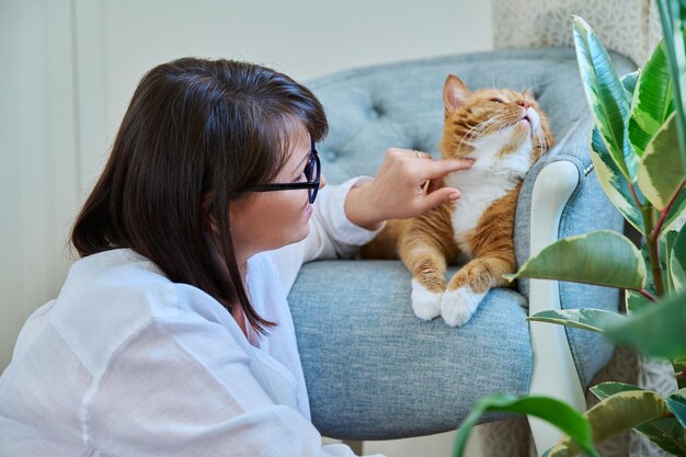 Mujer de mediana edad hablando tocando jengibre mascota gato casa interior fondo amistad amor cuidado ocio estilo de vida animales gente casa concepto