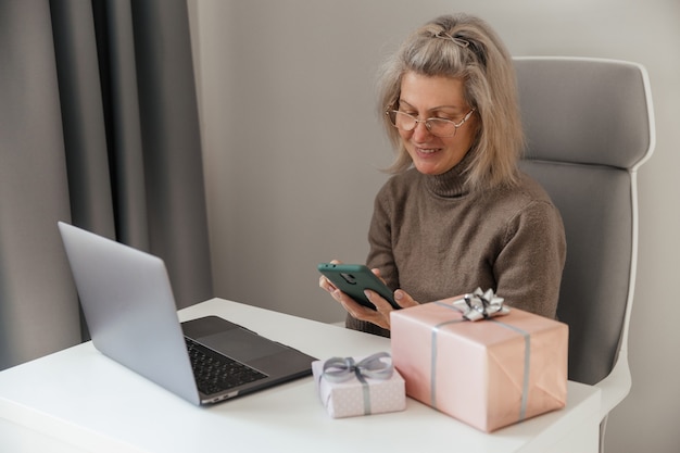 Una mujer de mediana edad hace pedidos y compras de regalos de Navidad por teléfono inteligente