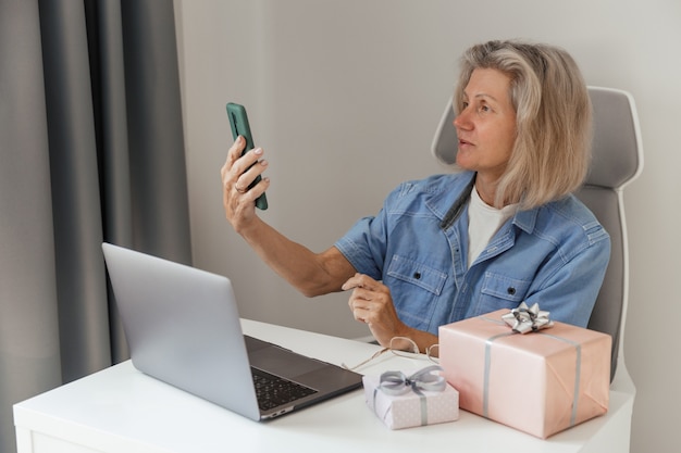 Foto una mujer de mediana edad hace pedidos y compras de regalos de navidad por teléfono inteligente