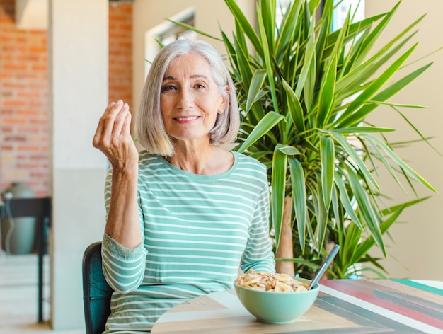 Mujer de mediana edad haciendo capice o gesto de dinero, ¡diciéndote que pagues tus deudas!