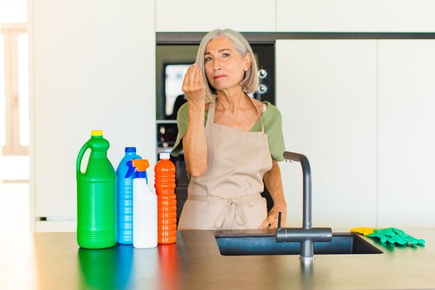 Mujer de mediana edad haciendo capice o gesto de dinero, ¡diciéndote que pagues tus deudas!