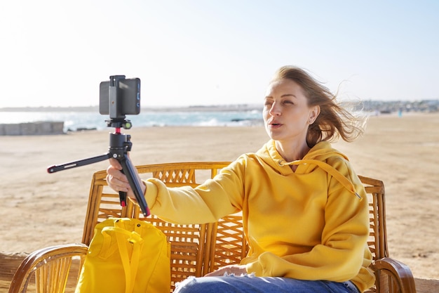 Mujer de mediana edad haciendo videollamadas en línea hablando riéndose del fondo del paisaje marino al atardecer