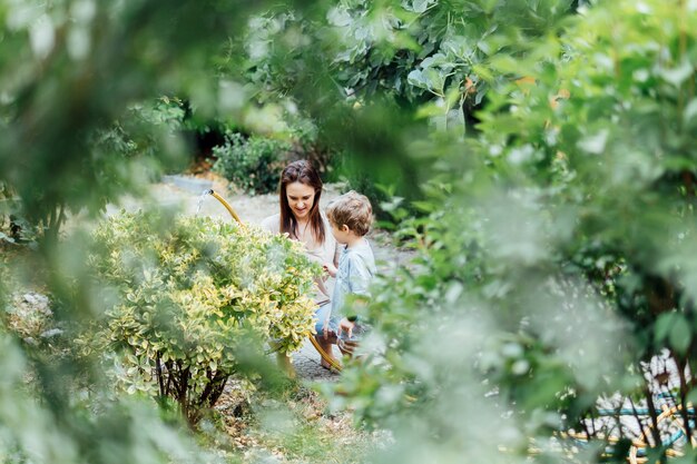 Mujer de mediana edad hermosa joven madre con su hijo de tres años en el jardín de su casa regando las plantas. tiempo familiar. familia monoparental, adopción lesbiana.