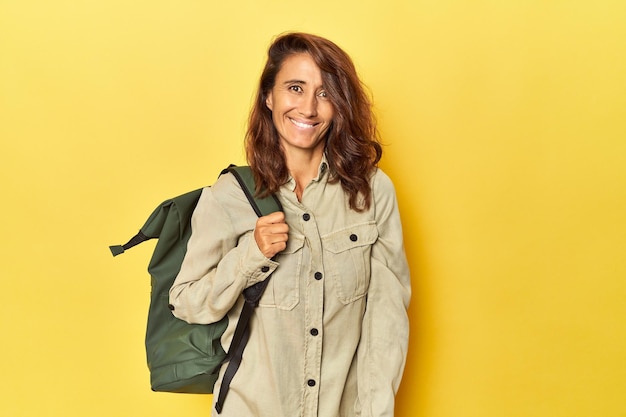 Mujer de mediana edad lista para viajar con mochila amarilla feliz sonriente y alegre