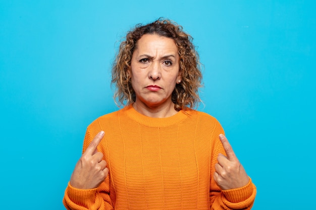 Mujer de mediana edad con una mala actitud que parece orgullosa y agresiva, apuntando hacia arriba o haciendo un signo divertido con las manos