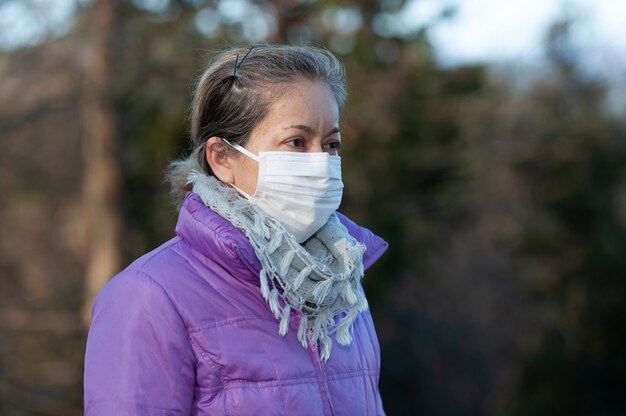 Foto mujer de mediana edad con una máscara quirúrgica blanca para protegerse contra el coronavirus