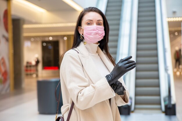 Mujer de mediana edad en mascarilla protectora poniéndose guantes con el telón de fondo de un lugar público