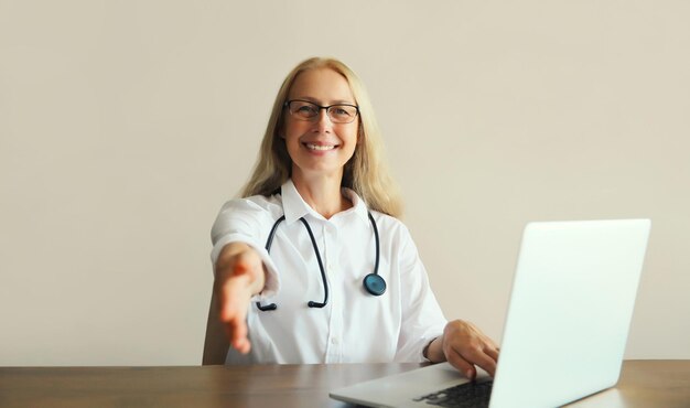 mujer de mediana edad médico trabajando con computadora portátil sentado en el escritorio en la oficina de la clínica médica