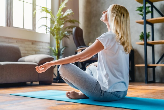 Mujer de mediana edad meditando en posición de loto mujer de edad practica yoga en casa
