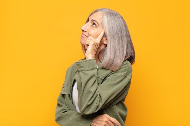 Mujer de mediana edad con mirada concentrada, preguntándose con expresión dudosa, mirando hacia arriba y hacia un lado