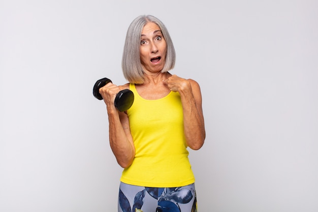 Mujer de mediana edad mirando consternado y sorprendido con la boca abierta, apuntando a sí mismo. concepto de fitness