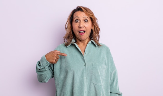 Mujer de mediana edad mirando consternado y sorprendido con la boca abierta, apuntando a sí mismo