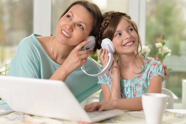 Mujer de mediana edad y niña escuchando música usando laptop