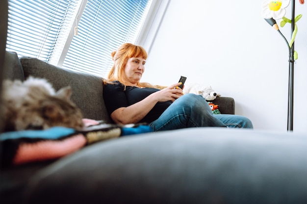 Foto mujer de mediana edad pasa tiempo usando el teléfono con su gato mascota