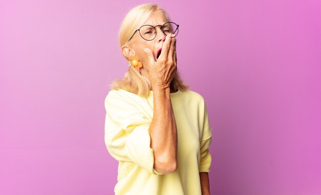 Mujer de mediana edad que bosteza perezosamente temprano en la mañana, se despierta y se ve somnolienta, cansada y aburrida