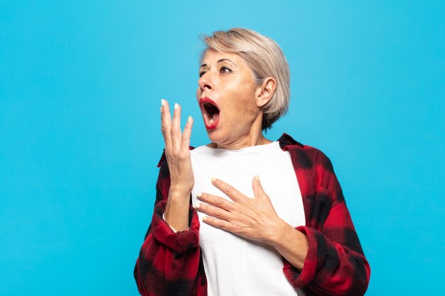 Mujer de mediana edad que bosteza perezosamente temprano en la mañana, se despierta y se ve somnolienta, cansada y aburrida