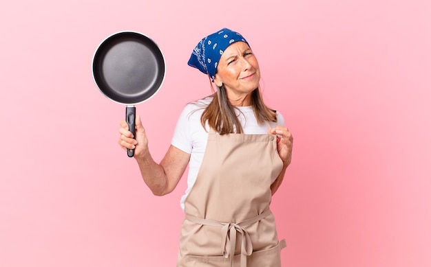 Mujer de mediana edad que parece arrogante, exitosa, positiva y orgullosa y sosteniendo una sartén. concepto de chef