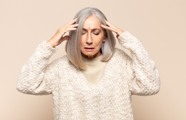 Mujer de mediana edad que parece concentrada, pensativa e inspirada, haciendo una lluvia de ideas e imaginando con las manos en la frente