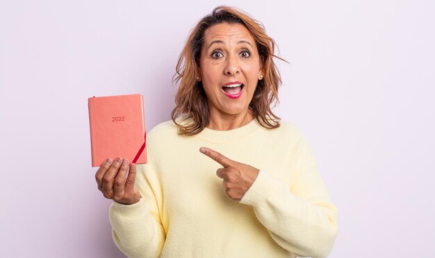 Mujer de mediana edad que parece emocionada y sorprendida apuntando hacia el lado. concepto de agenda