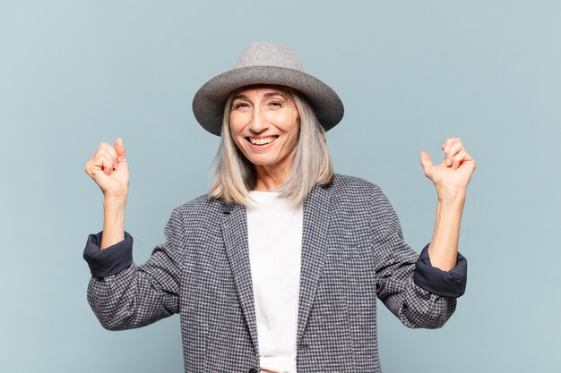 Mujer de mediana edad que parece extremadamente feliz y sorprendida, celebrando el éxito, gritando y saltando