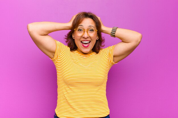 Foto mujer de mediana edad que parece feliz, despreocupada, amigable y relajada disfrutando de la vida y el éxito, con una actitud positiva contra la pared púrpura