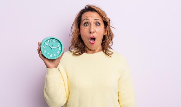 Mujer de mediana edad que parece muy conmocionada o sorprendida. concepto de reloj despertador