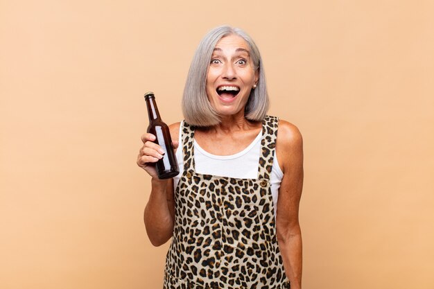 Mujer de mediana edad que parece muy conmocionada o sorprendida, mirando con la boca abierta diciendo wow con una cerveza