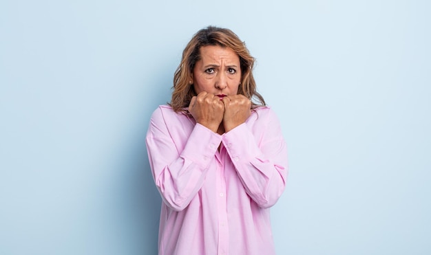 Mujer de mediana edad que parece preocupada, ansiosa, estresada y asustada, mordiéndose las uñas y mirando al espacio de copia lateral