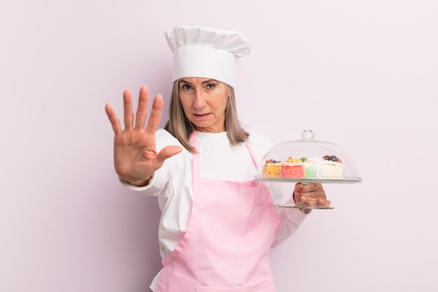 Mujer de mediana edad que parece seria mostrando la palma abierta haciendo un gesto de parada concepto de panadero y pasteles