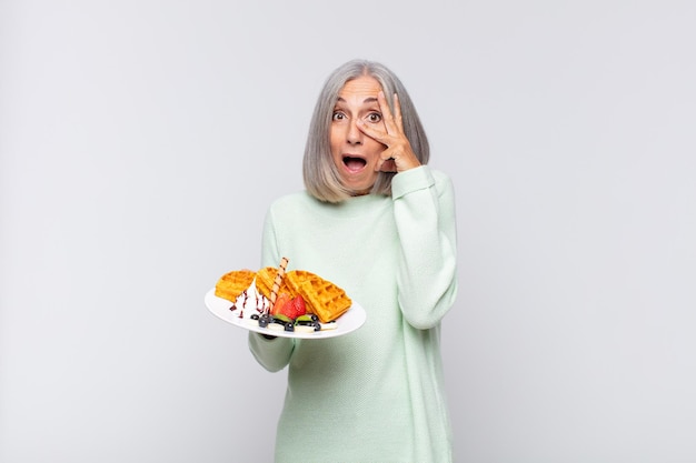 Mujer de mediana edad que parece sorprendida, asustada o aterrorizada, cubriendo la cara con la mano y mirando entre los dedos. concepto de desayuno