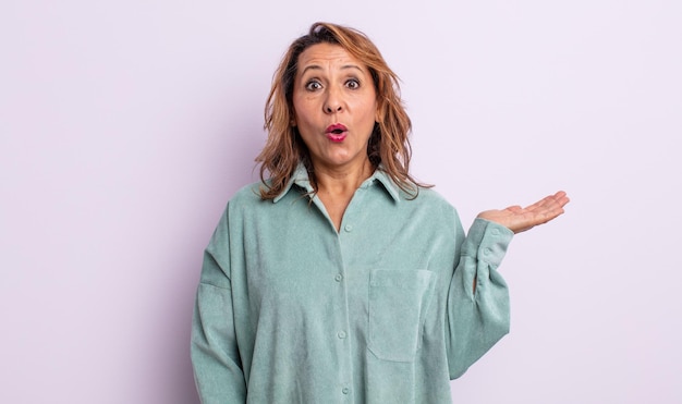 Mujer de mediana edad que parece sorprendida y conmocionada, con la mandíbula caída sosteniendo un objeto con la mano abierta en el costado