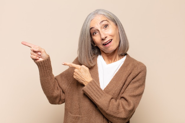 Mujer de mediana edad que se siente alegre y sorprendida, sonriendo con una expresión de sorpresa y apuntando hacia un lado