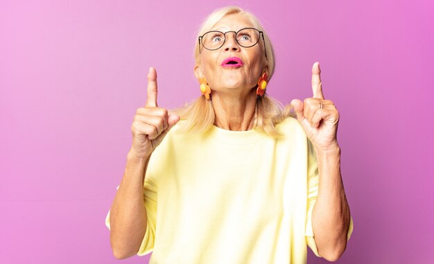 Mujer de mediana edad que se siente asombrada y con la boca abierta apuntando hacia arriba con una mirada de asombro y sorpresa