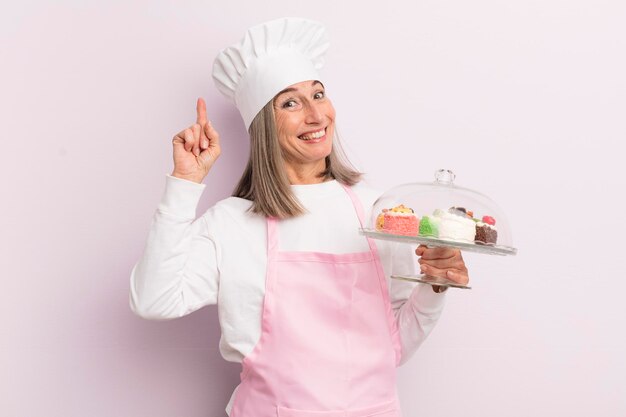 Mujer de mediana edad que se siente como un genio feliz y emocionado después de darse cuenta de una idea del concepto de panadero y pasteles