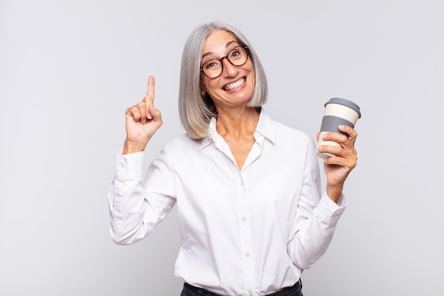 Mujer de mediana edad que se siente como un genio feliz y emocionado después de realizar una idea, levantando alegremente el dedo, ¡eureka! concepto de cafe