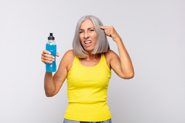 Mujer de mediana edad que se siente confundida y perpleja, mostrando que estás loco, loco o loco. concepto de fitness