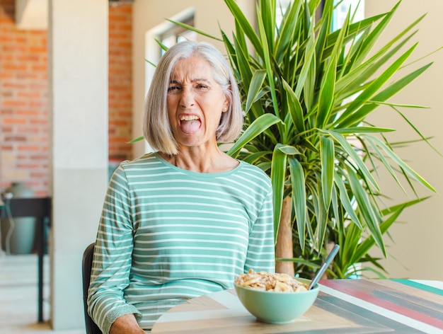 Mujer de mediana edad que se siente disgustada e irritada, que saca la lengua, no le gusta algo desagradable y asqueroso