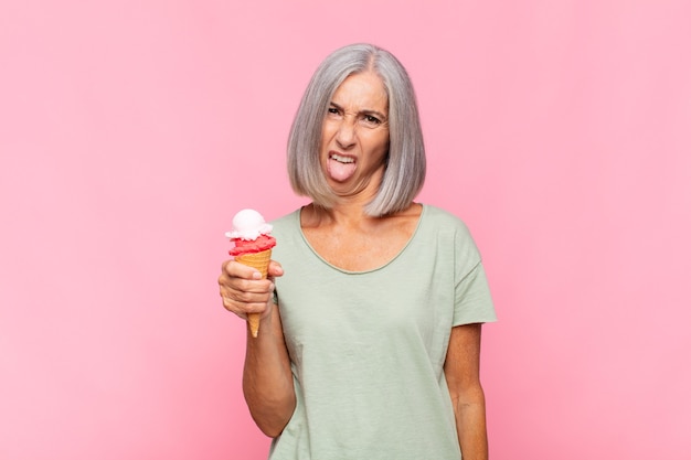 Mujer de mediana edad que se siente disgustada e irritada, sacando la lengua, disgustando algo desagradable y asqueroso tomando un helado