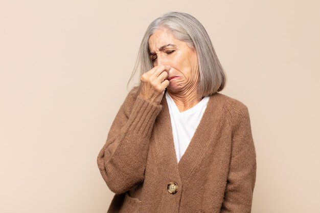 Mujer de mediana edad que se siente disgustada, tapándose la nariz para evitar oler un hedor desagradable y desagradable