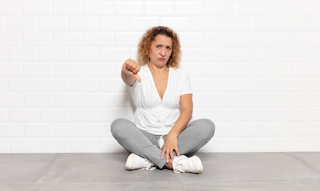 Mujer de mediana edad que se siente enfadada, enojada, molesta, decepcionada o disgustada, mostrando el pulgar hacia abajo con una mirada seria