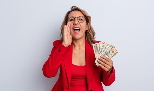 Mujer de mediana edad que se siente feliz, dando un gran grito con las manos al lado de la boca. concepto de billetes de dólar