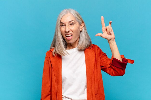 Mujer de mediana edad que se siente feliz, divertida, segura, positiva y rebelde, haciendo un letrero de rock o heavy metal con la mano