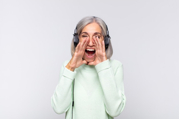 Mujer de mediana edad que se siente feliz, emocionada y positiva, dando un gran grito con las manos al lado de la boca, gritando. concepto de musica