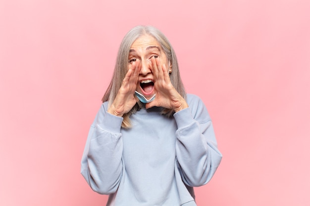 Mujer de mediana edad que se siente feliz, emocionada y positiva, dando un gran grito con las manos al lado de la boca, gritando